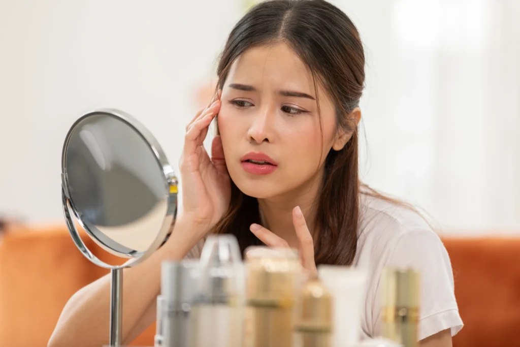 Woman examining her face in a mirror | Gretchen W Frieling MD